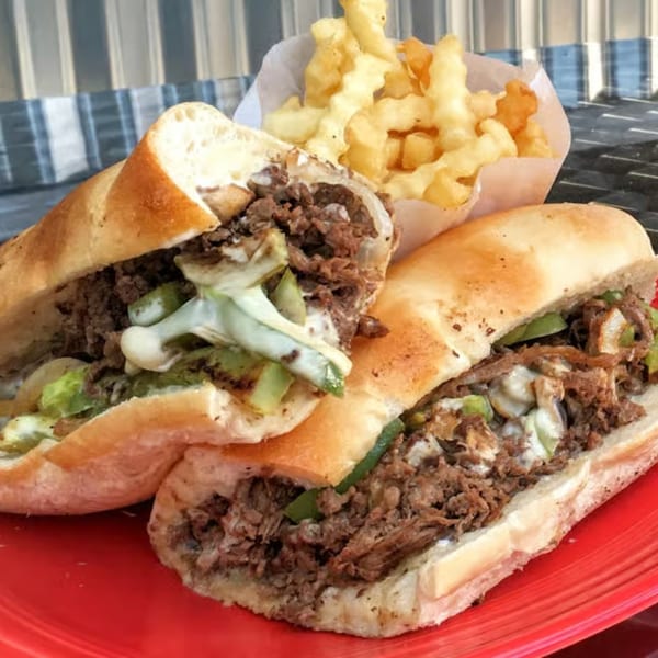 Two Bruchi's cheesesteak subs with steak, onions, peppers, and cheese, alongside crinkle-cut fries.