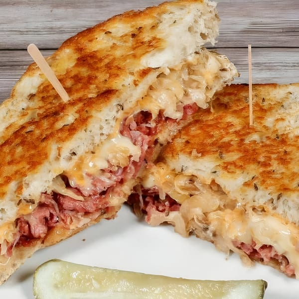 A Bruchi's grilled pastrami and cheese sandwich, cut in half, with a pickle spear.