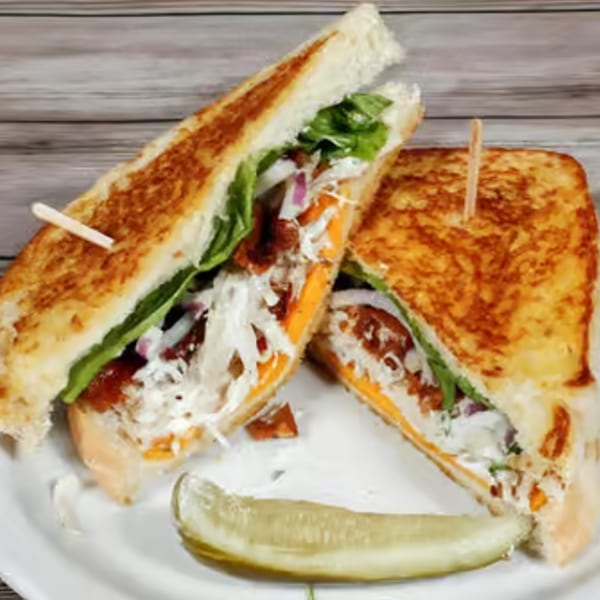 Two halves of a grilled sandwich with cheese, lettuce, and meat, served with a pickle spear.