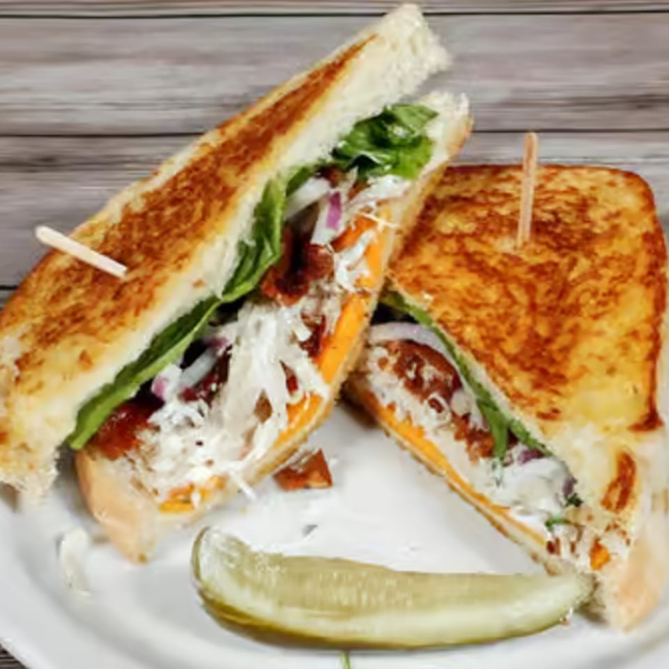 Two halves of a grilled sandwich with cheese, lettuce, and meat, served with a pickle spear.