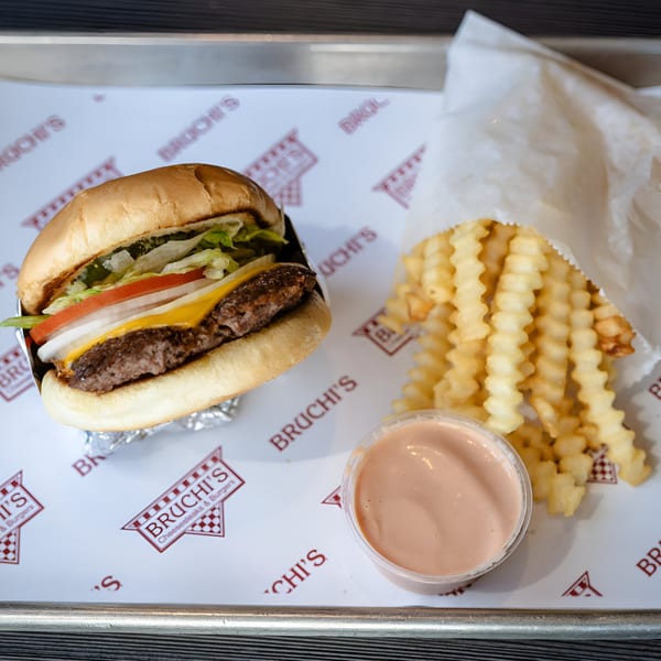 Bruchi's cheeseburger with lettuce, tomato, onion, and cheese, served with crinkle-cut fries and dipping sauce.