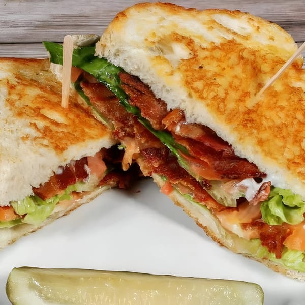 Bruchi's BLT sandwich with crispy bacon, lettuce, tomato, and a pickle spear on a white plate.