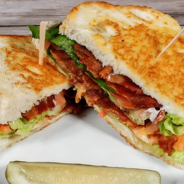 A Bruchi's BLT sandwich, cut in half, with crispy bacon, lettuce, tomato, and a pickle spear.