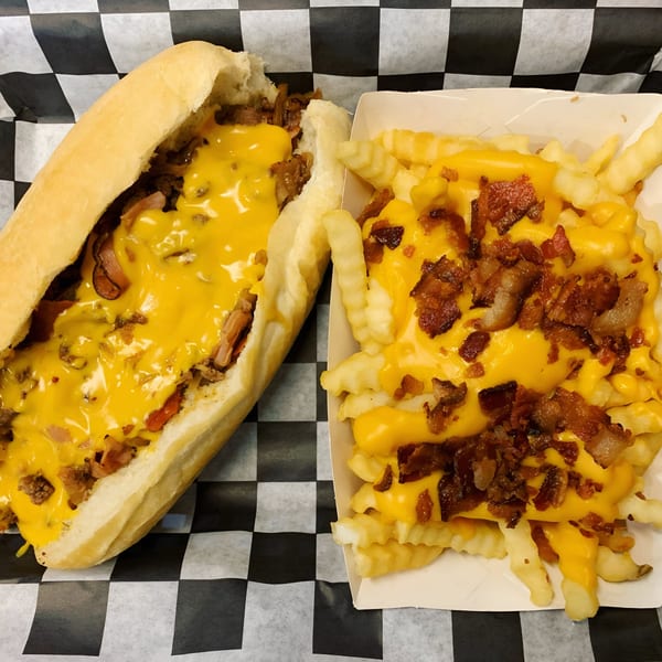 Bruchi's cheesesteak sandwich with melted cheese and a side of cheese fries with bacon bits.