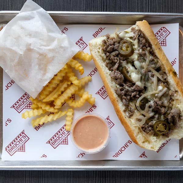 Bruchi's cheesesteak with jalapeños, crinkle-cut fries, and dipping sauce on a branded tray liner.